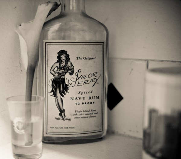 A black and white photo of Sailor Jerry Spiced Navy Rum with a lily in a glass in the foreground