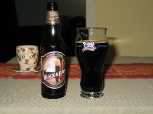 A bottle of Sam Adams Black and Brew beer next to a Samuel Adams specialty beer glass filled with the dark Black and Brew stout.