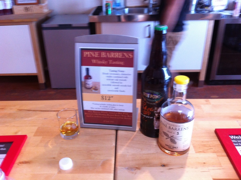 20120817-170048.jpg A shot glass with Long Island Spirits Pine Barrens Whisky, next to a sign with a description of the tasting, a bottle of Blue Point Brewing Old Howling Bastard barleywine, and a bottle of Pine Barrens Whisky.