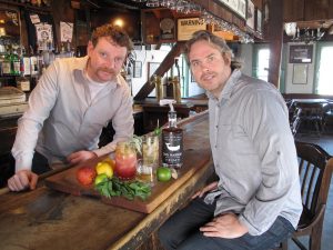 Mike McQuade and Jason Laan sit at a bar with a bottle of Old Whalers Style Sag Harbor Hand Crafted Rum