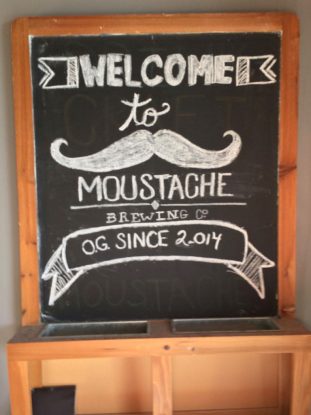 Chalk board at entrance of Moustache Brewing Co in Riverhead, NY, with writing welcoming customers