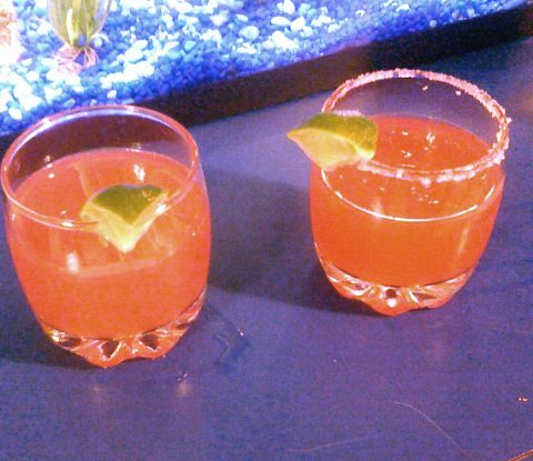 Two glasses with Cranberry Margaritas and lime wedges. The glass on the right has a salted rim.