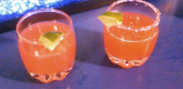 Two glasses with Cranberry Margaritas and lime wedges. The glass on the right has a salted rim.