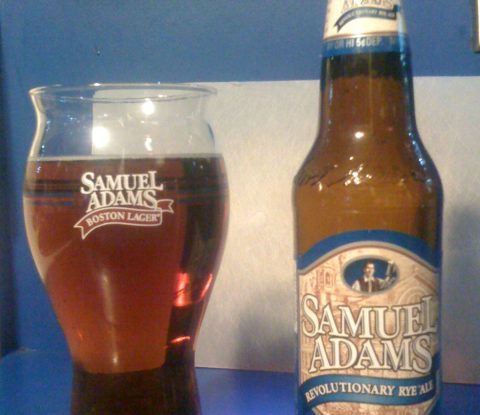 Samuel Adams Revolutionary Rye Ale poured into a glass, next to the bottle.