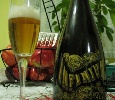 A fluted glass containing Samuel Adams Infinium next to a bottle of Samuel Adams Infinium