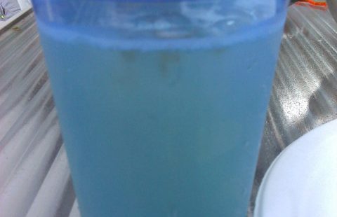 A blue plastic cup filled with a Lillet spritzer. An orange paper umbrella is hanging over the rim.