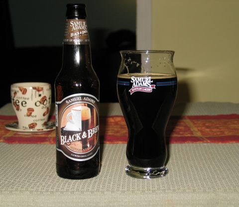 A bottle of Sam Adams Black and Brew beer next to a Samuel Adams specialty beer glass filled with the dark Black and Brew stout.