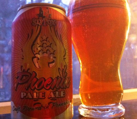 A can of SlyFox Phoenix Pale Ale and the beer poured into a pint glass. The beer is dark amber in color.