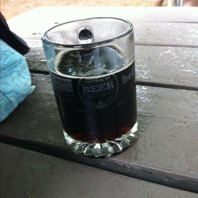 A Toronto’s Festival of Beer glass mug partly filled with Krombacher Dark on a wooden picnic table.
